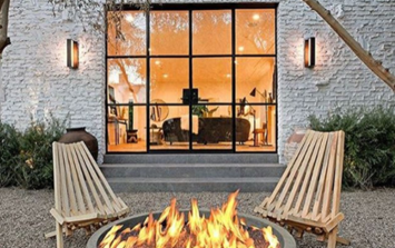 An outdoor fireplace with wooden chairs and exterior steel door from Pinky's Iron Doors