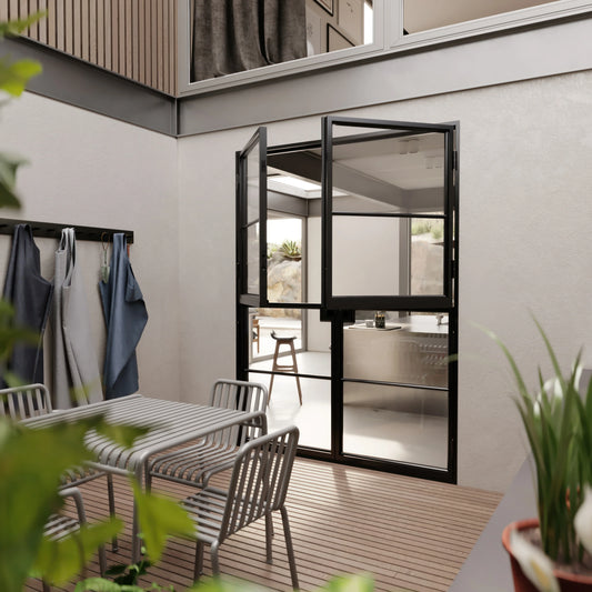 Black-framed glass double doors open from a modern patio with a dining set into a bright interior space with minimalist decor