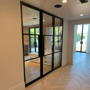 A pair of modern glass and steel double doors with a right sidelight in a bright, airy luxury home.