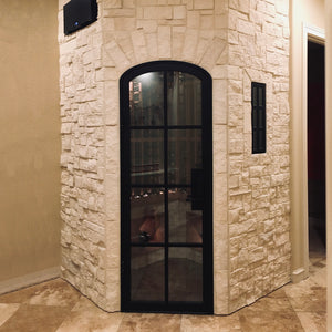 A minimalist arch top steel door fronting a luxurious stone wine cellar