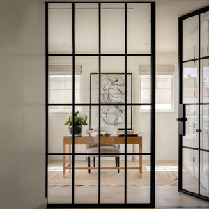 An artsy home office seen through an interior glass and steel wall partition and steel door